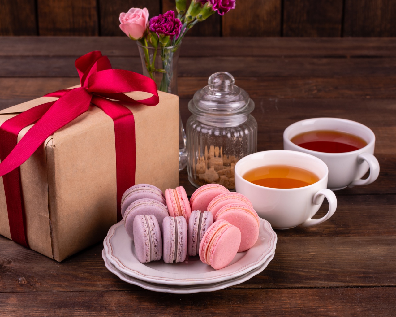 Подарок с красной лентой на столе с макарунами и чаем 