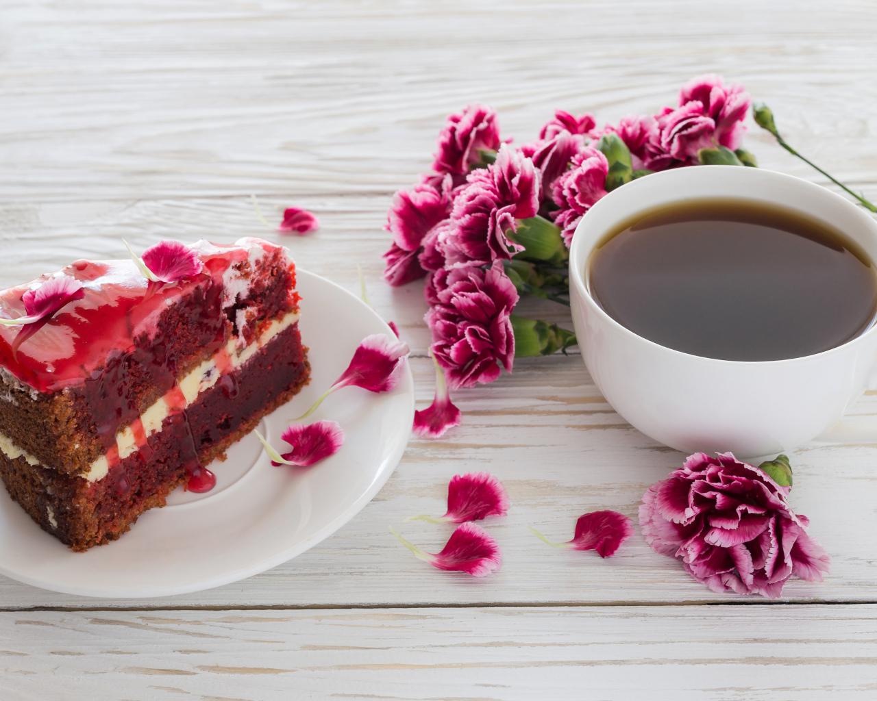 Кусок торта на столе с букетом гвоздик и чашкой кофе