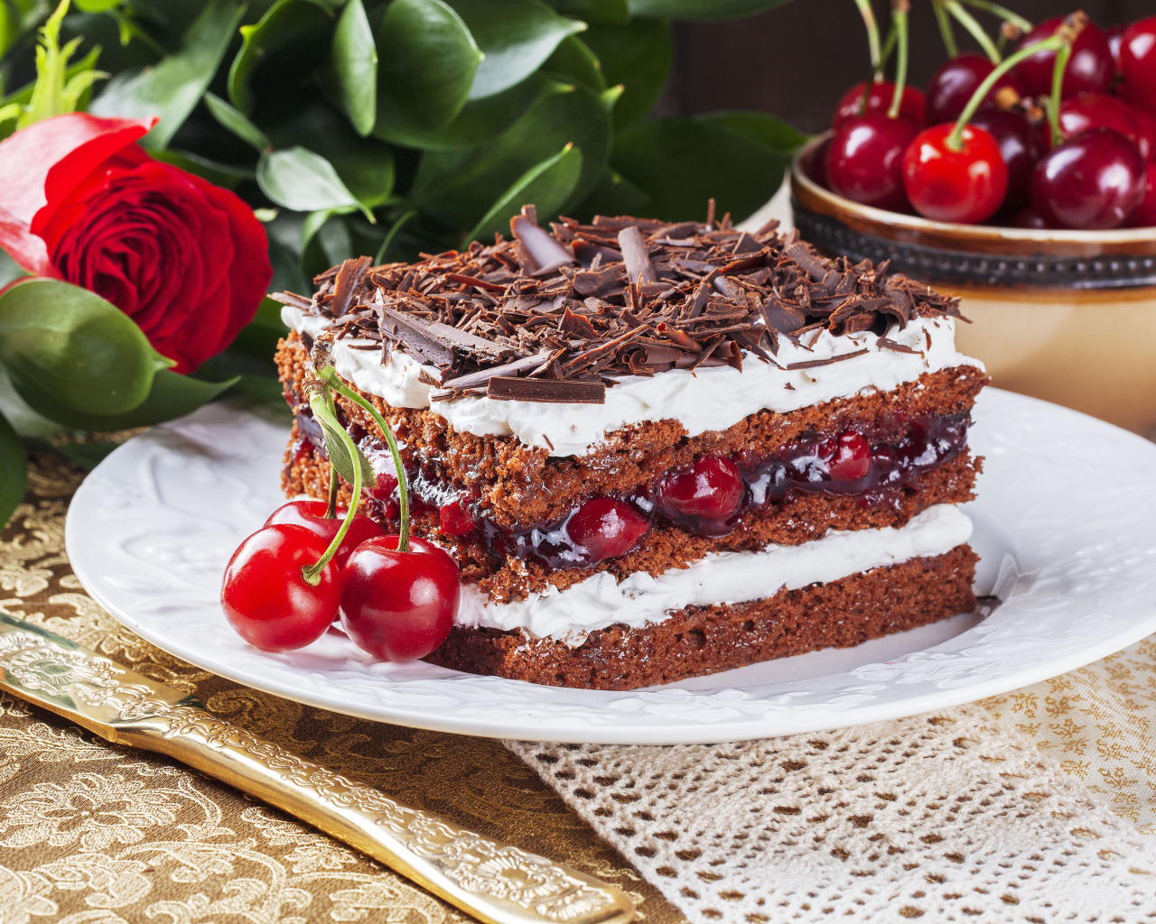 Кусок торта с вишней, шоколадной крошкой на столе с розой