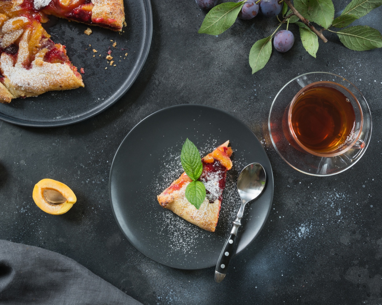 Кусок пирога с сахарной пудрой и абрикосами и сливами на столе с чаем 