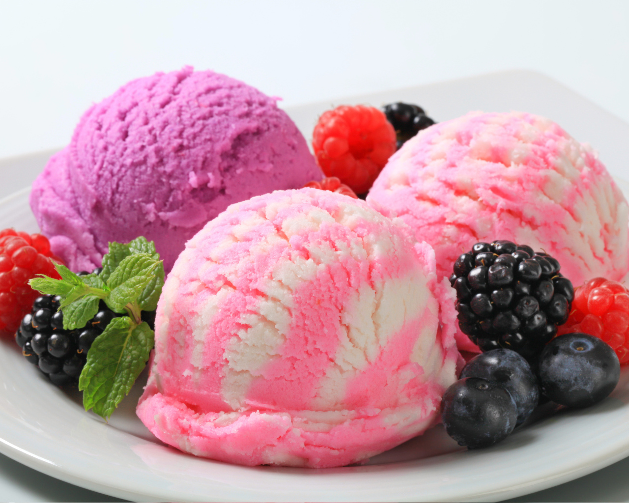 Шарики фруктового мороженого на белой тарелке с ягодами