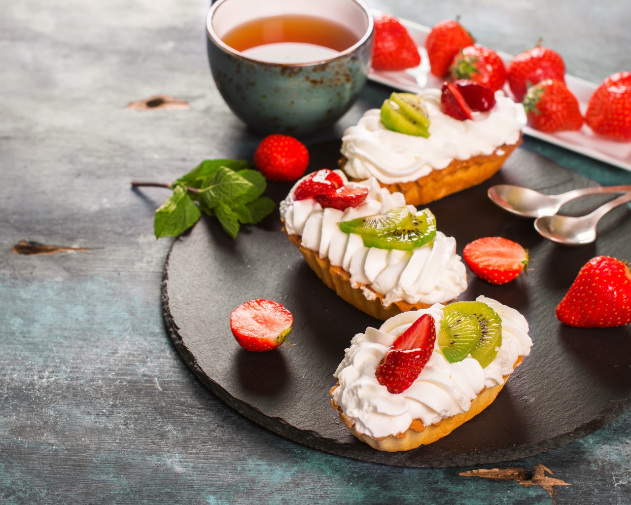 Пирожные с киви и клубникой на столе с чаем