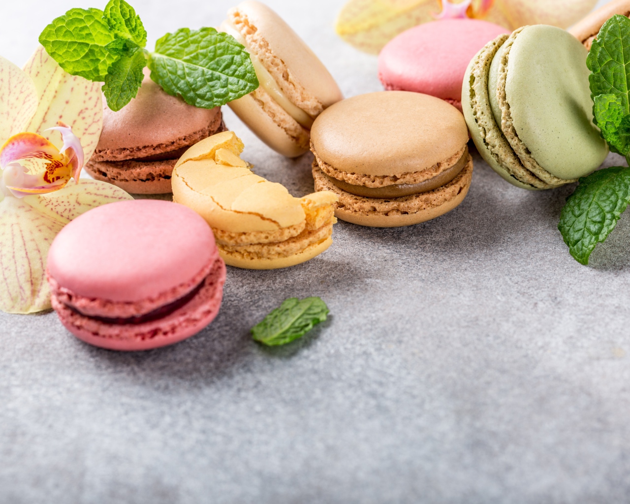 Десерт макарон на серой поверхности с цветами орхидеи и мятой