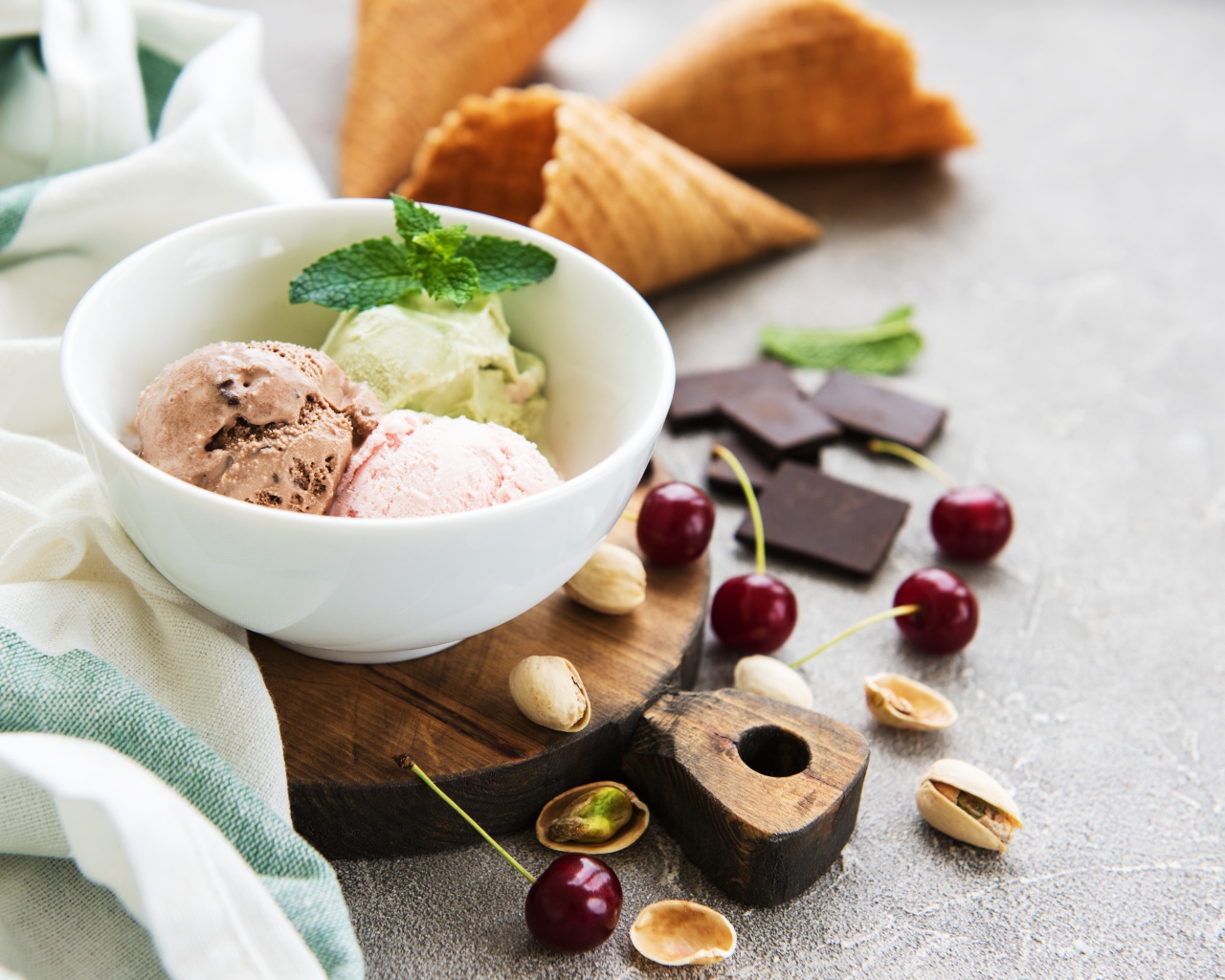 Шарики мороженого на столе вафельными рожками, черешней и фисташками