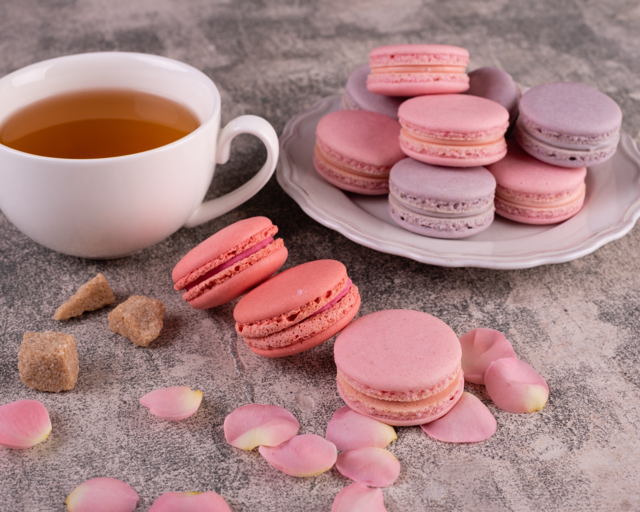 Сладкий десерт макарун на столе с чашкой чая, сахаром и лепестками розы