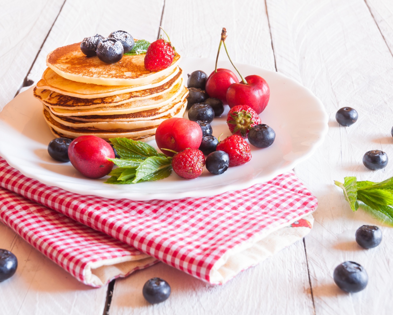 Оладья на белой тарелке с ягодами черники, черешни и клубники