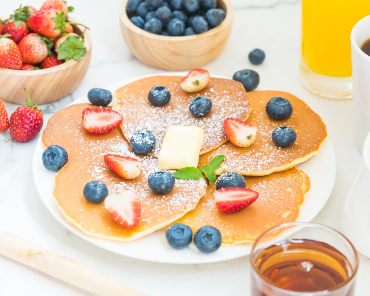 Оладьи с сахарной пудрой, клубникой и черникой на столе