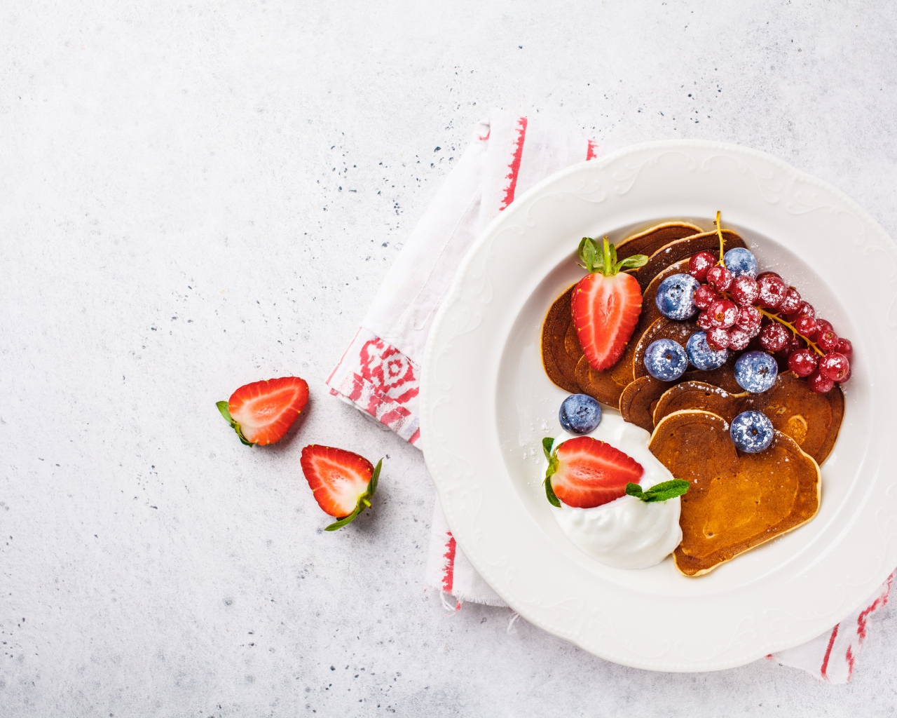 Оладьи со сметаной в тарелке с ягодами черники, клубники и красной смородины