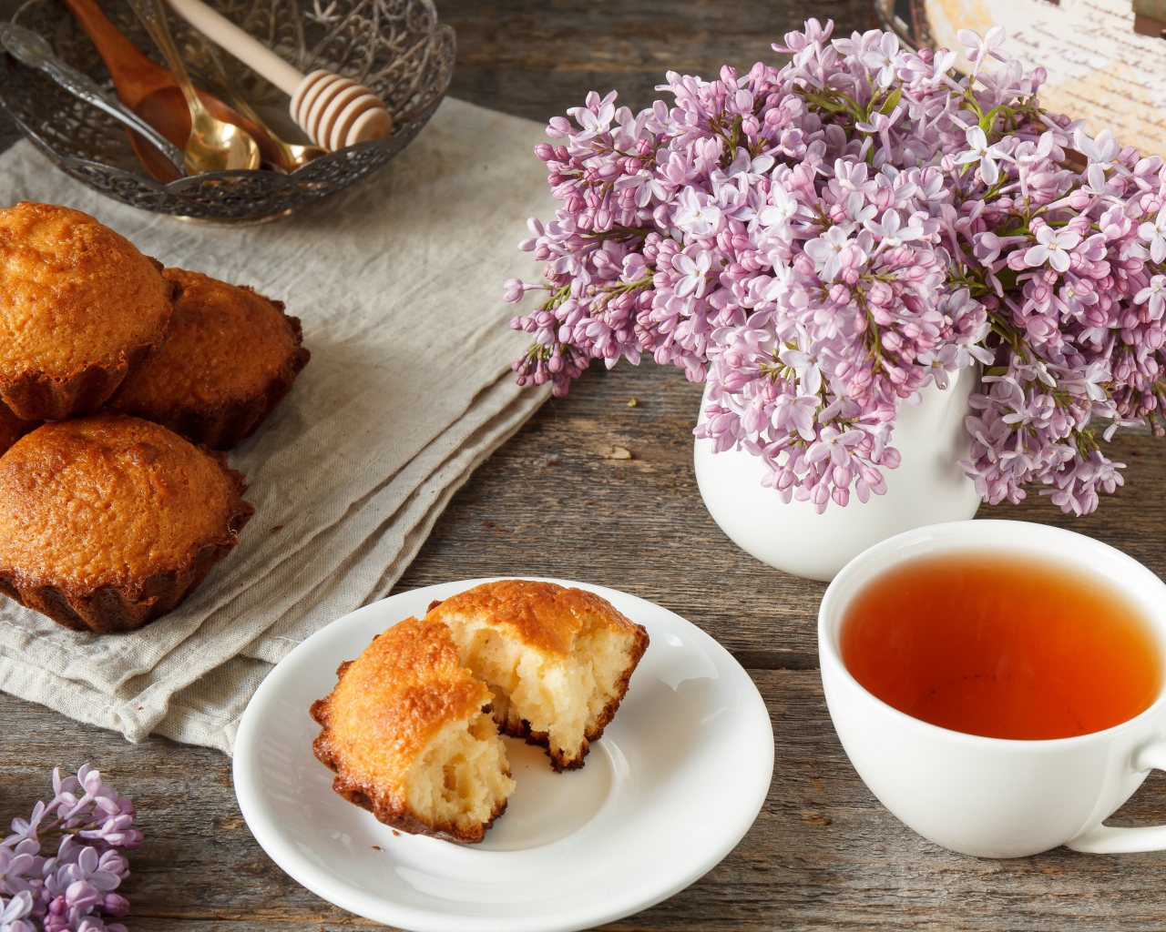 Сладкие кексы на столе с чаем и букетом сирени