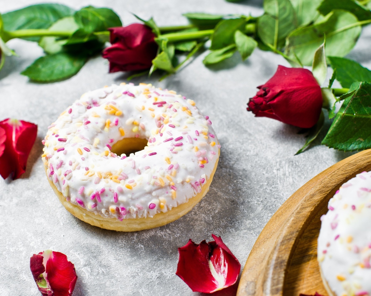 Сладкий пончик с глазурью на столе с красными розами