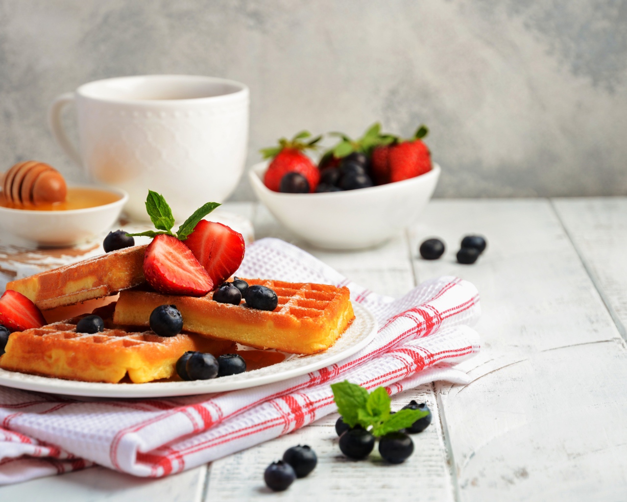 Сладкие вафли с ягодами черники и клубники на столе с медом и чаем