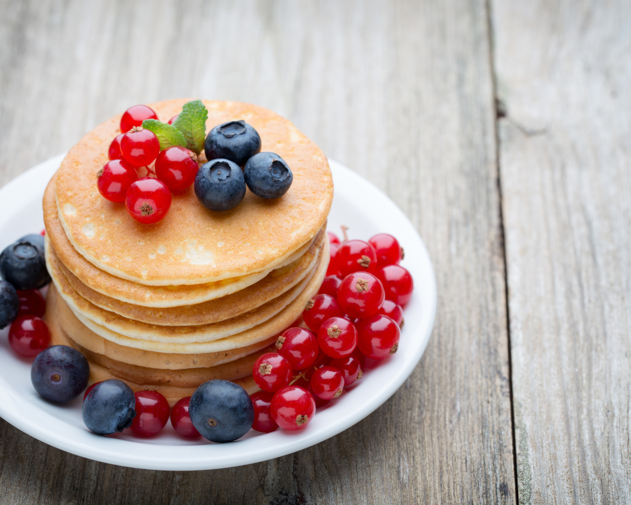Вкусные оладьи на тарелке с ягодами красной смородины и черники