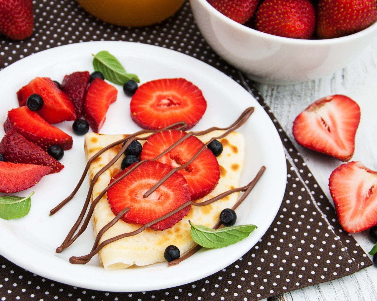 Тонкий блинчик на тарелке с шоколадом, ягодами клубники и черники