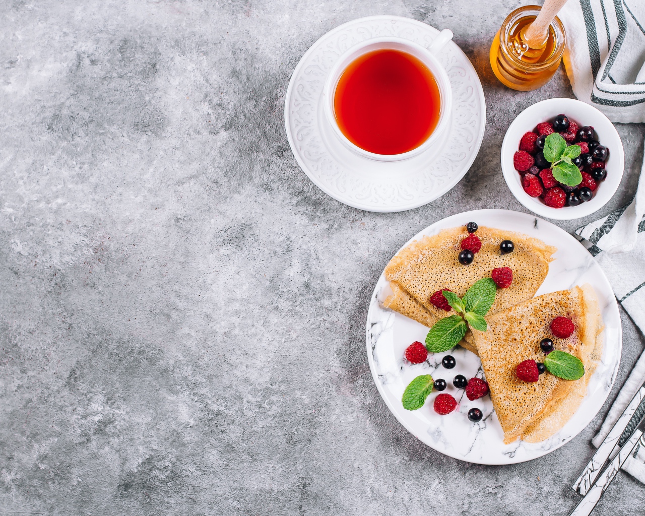 Тонкие блинчики на столе с ягодами, чаем и медом