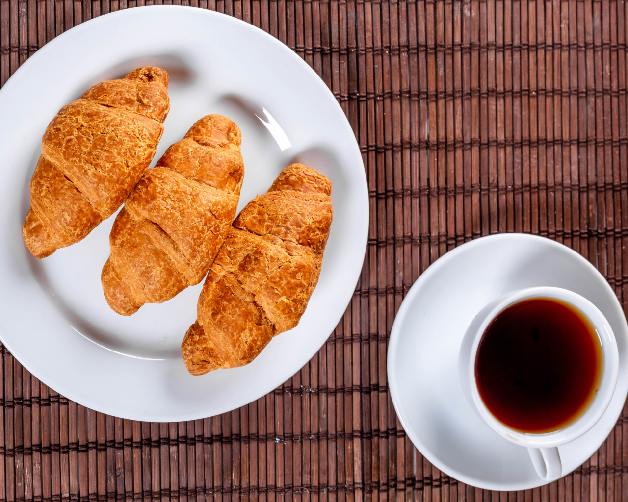 Три круассана на белой тарелке на столе с чаем