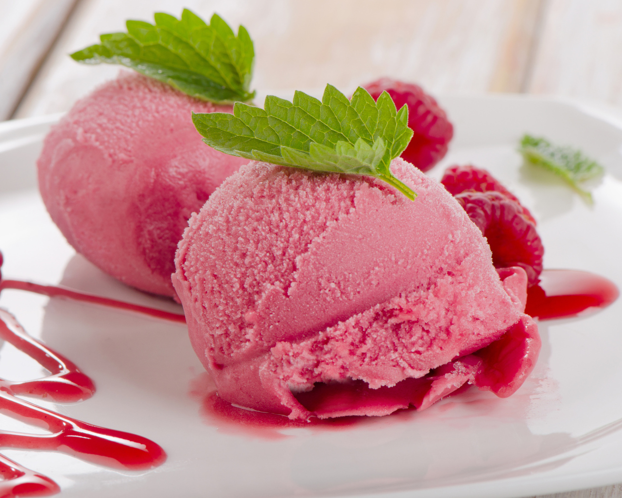 Два шарика малинового мороженого на тарелке с ягодами 