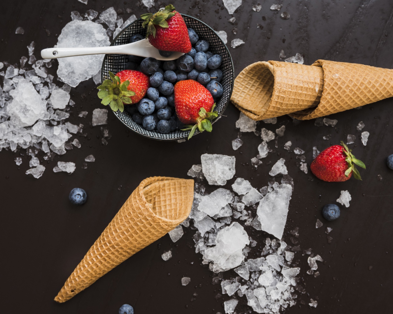 Вафельные рожки на столе со льдом и ягодами черники и клубники