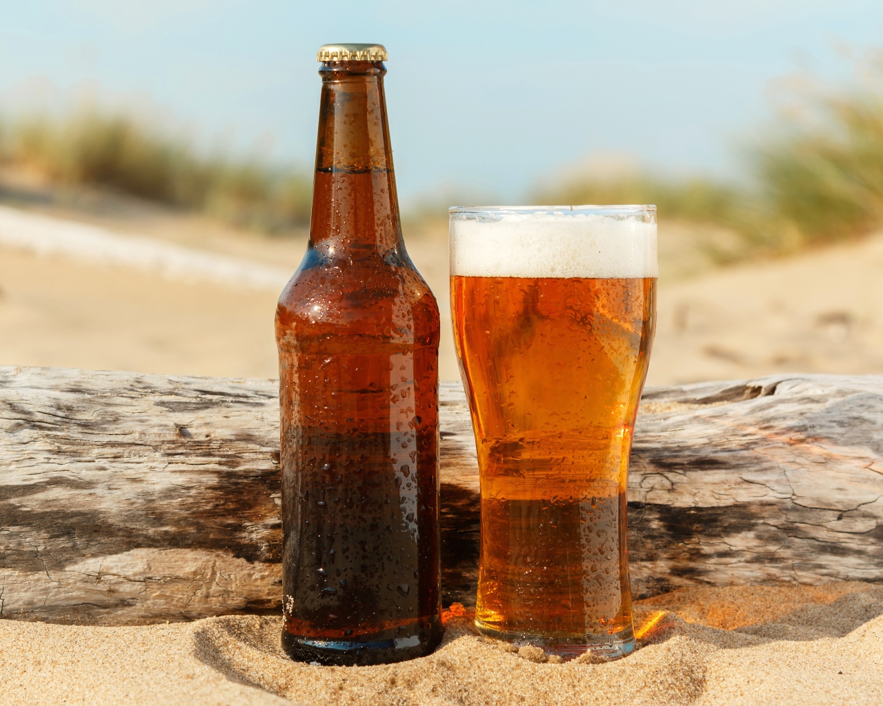 Бутылка пива и бокал стоят на песке 