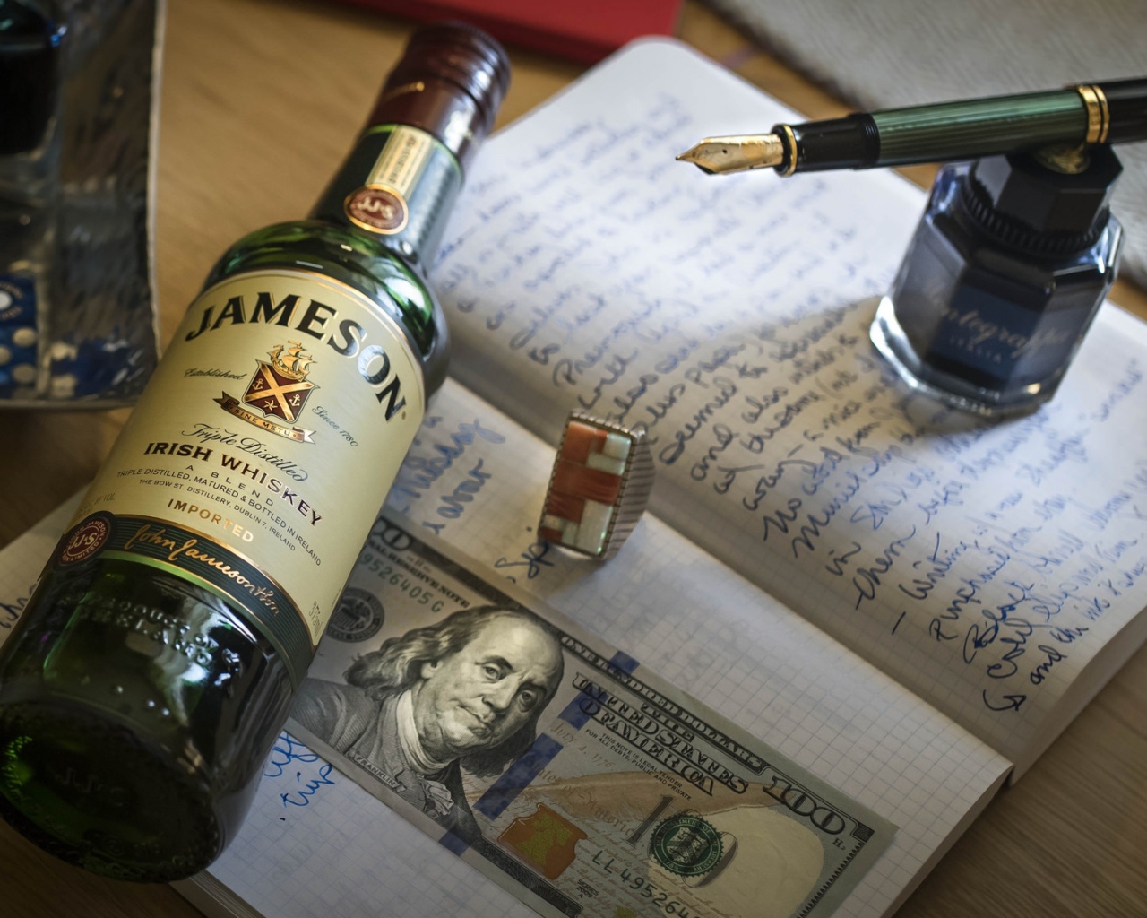 Бутылка виски лежит на тетради с чернильницей и купюрой