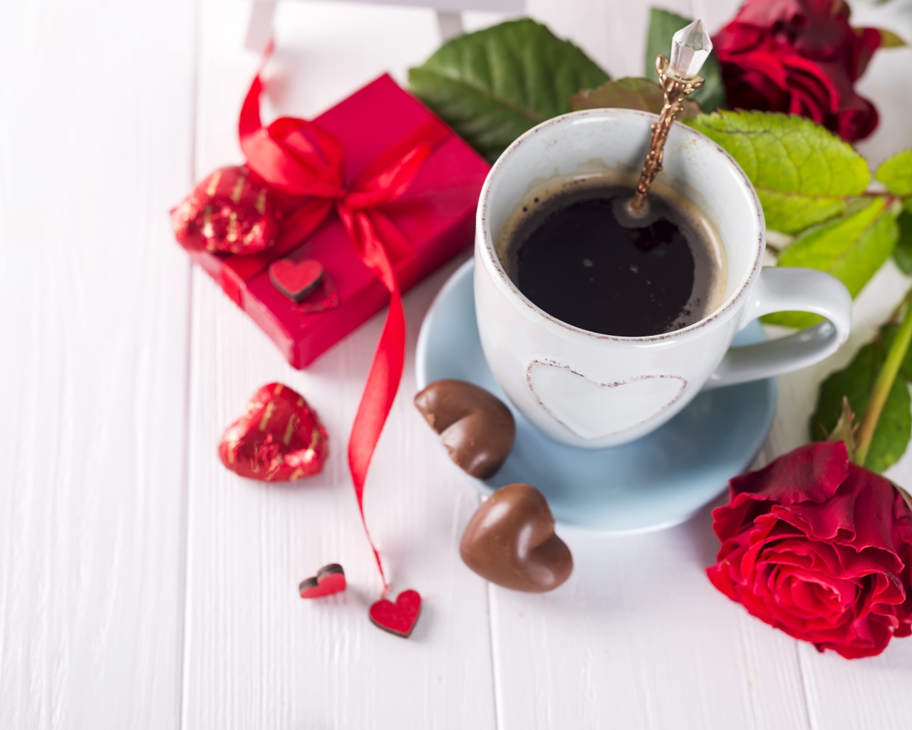 Чашка кофе на столе с шоколадными конфетами, подарком и красной розой