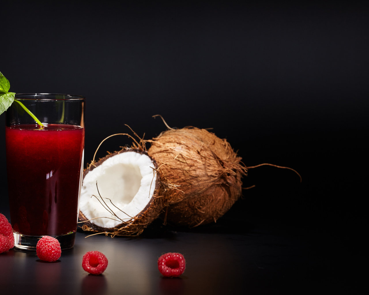 Стакан сока на столе с кокосом и ягодами малины 