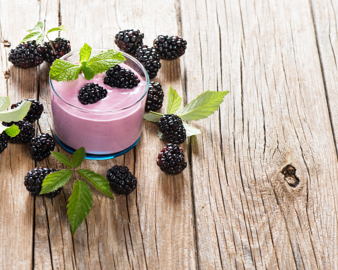 Стакан йогурта на деревянном столе с ягодами ежевики