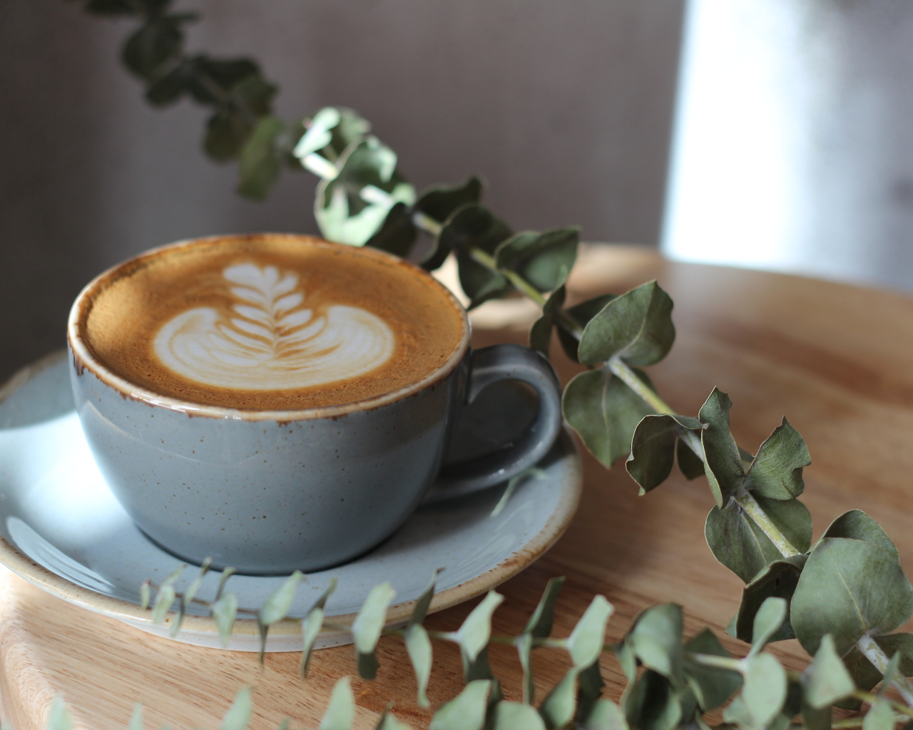 Большая чашка кофе с рисунком на пене на столе с веткой