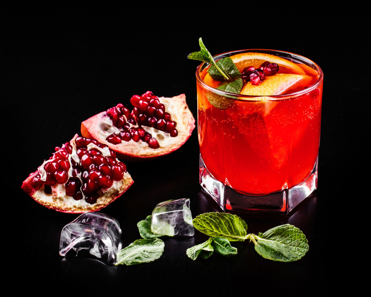 Алкогольный напиток в стакане на черном фоне с гранатом, кусочками льда и мятой