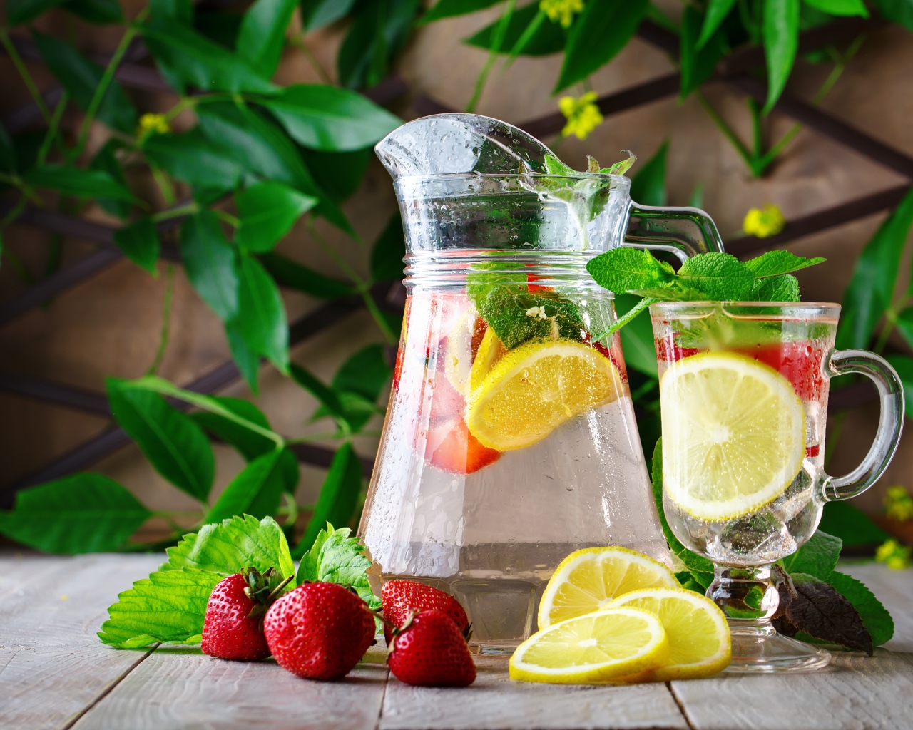 Холодный мохито в графине на столе с клубникой и лимоном