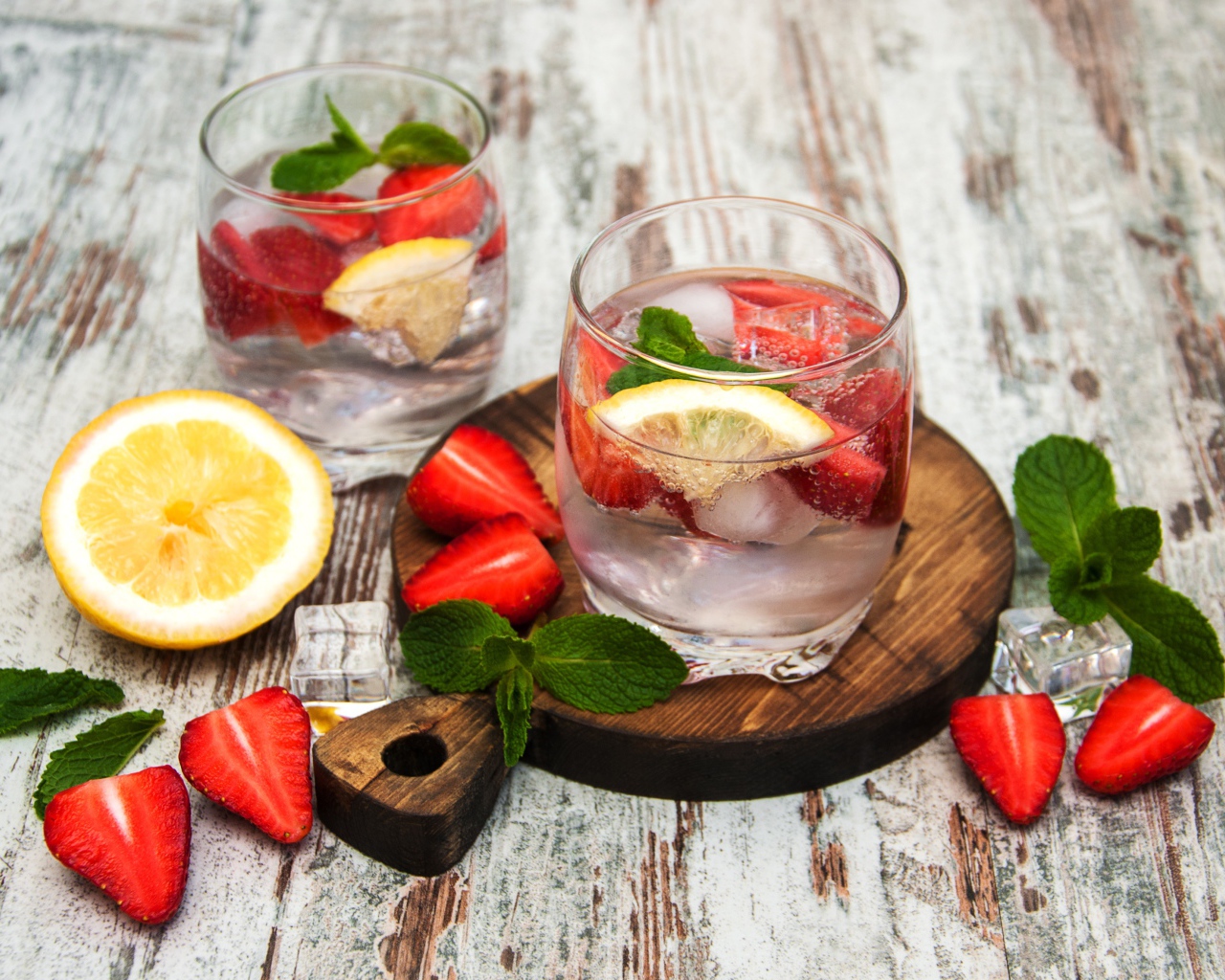 Холодный мохито на столе с ягодами клубники, лимоном и мятой