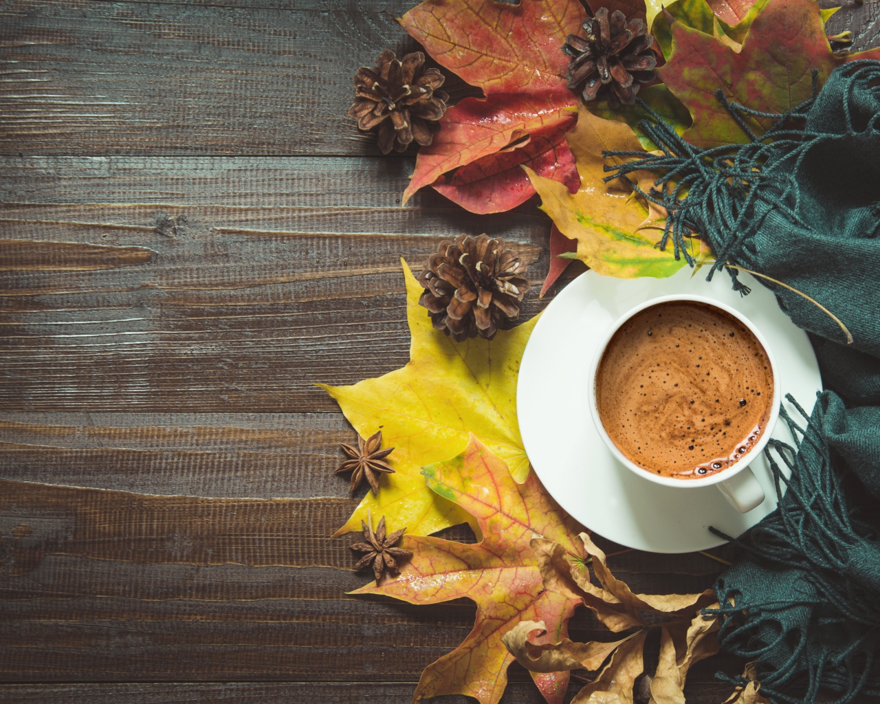 Чашка кофе на столе с шарфом, желтыми листьями и шишками