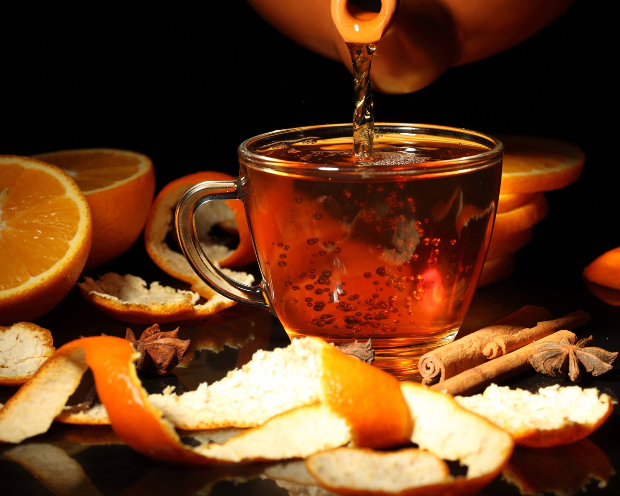 Стеклянная чашка с чаем на столе с апельсинами и корицей