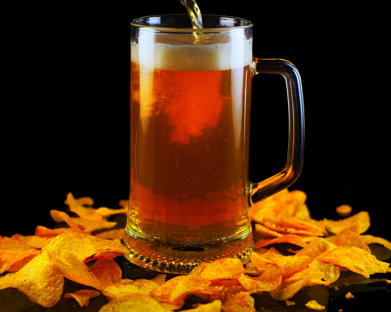 Бокал пива с чипсами на черном фоне