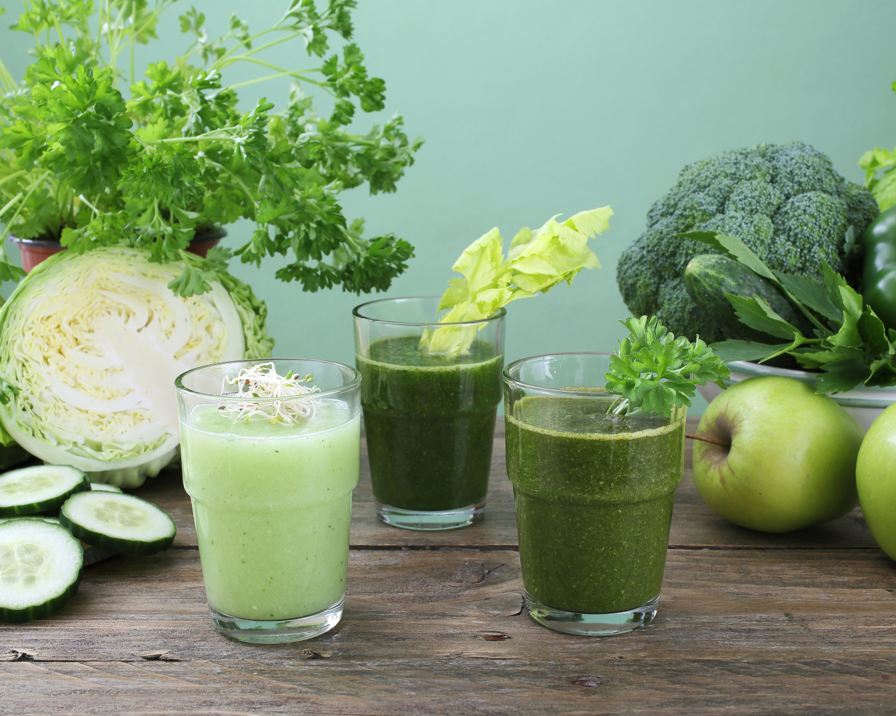 Зеленый овощной смузи в стаканах на столе со свежими овощами и яблоками