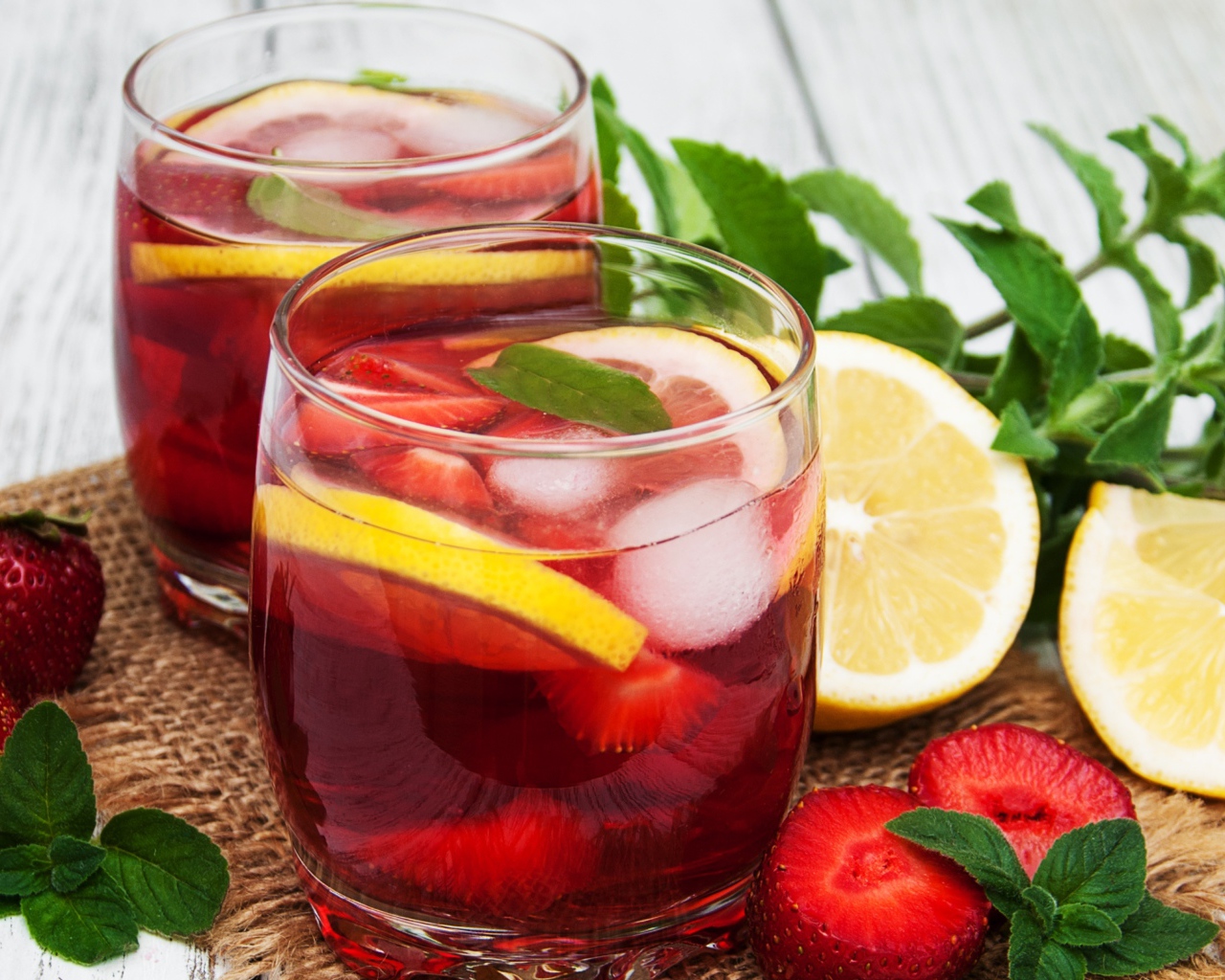 Мохито в стаканах на столе с клубникой, лимоном и мятой