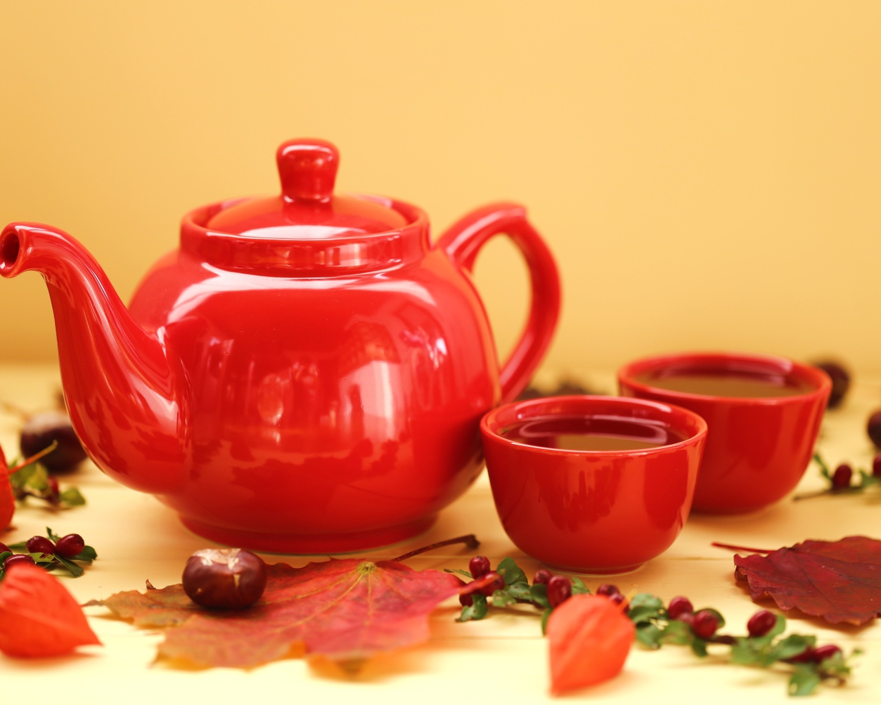 Красный чайник с чашками на столе осенью 