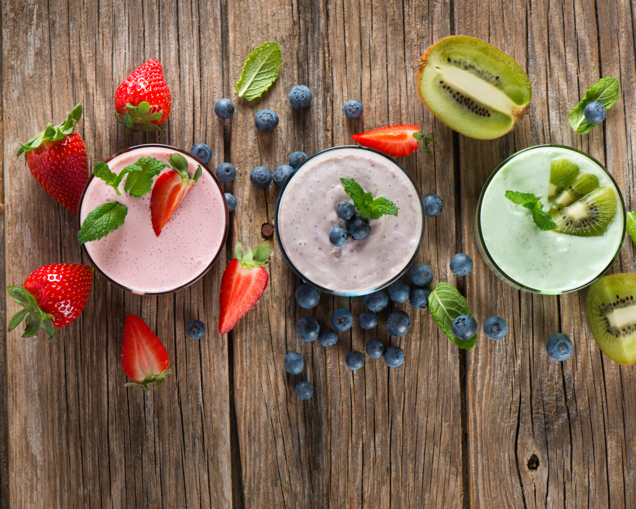 Стаканы со смузи на столе с киви, ягодами клубники и черники