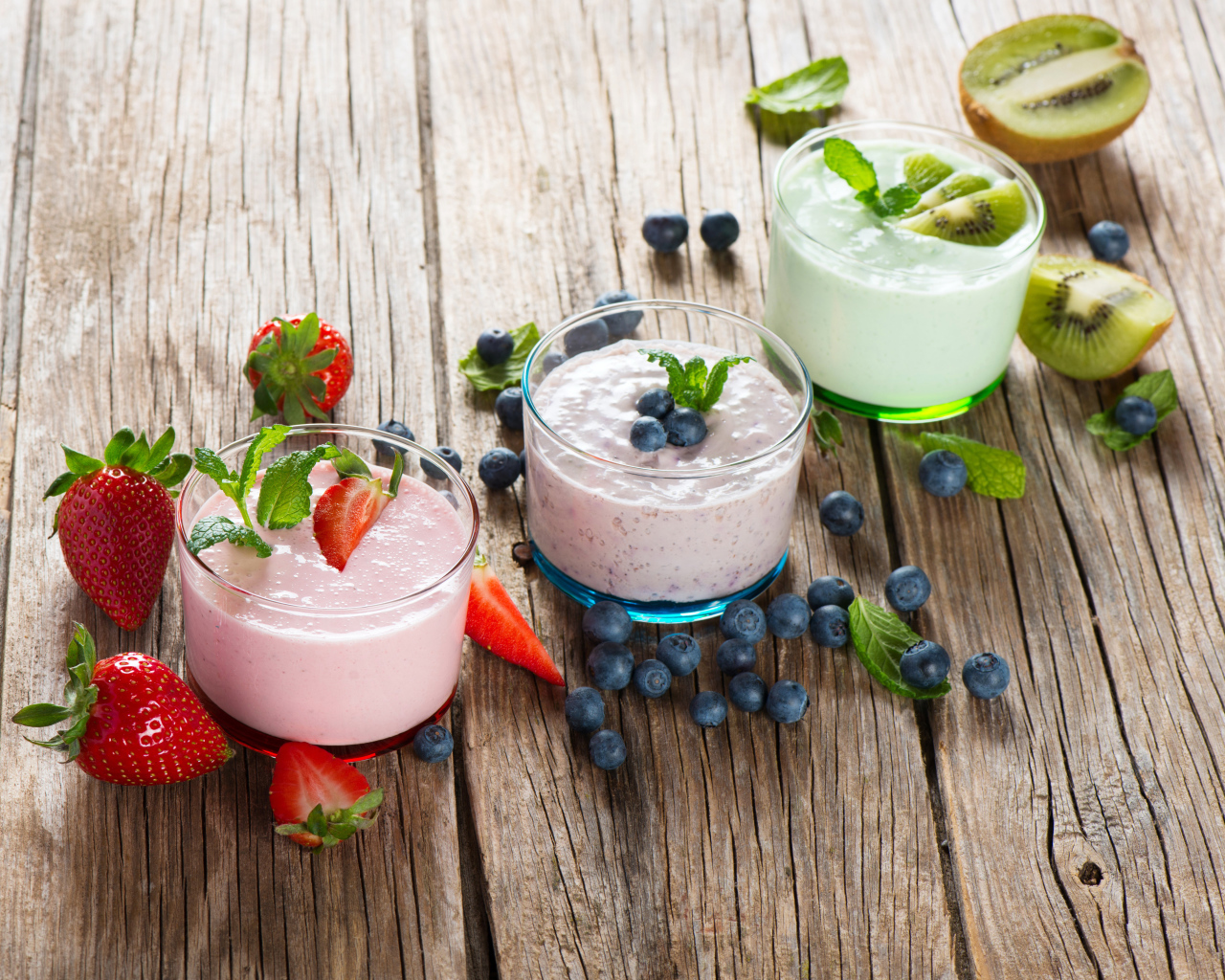 Three glasses of smoothies with berries on a wooden table