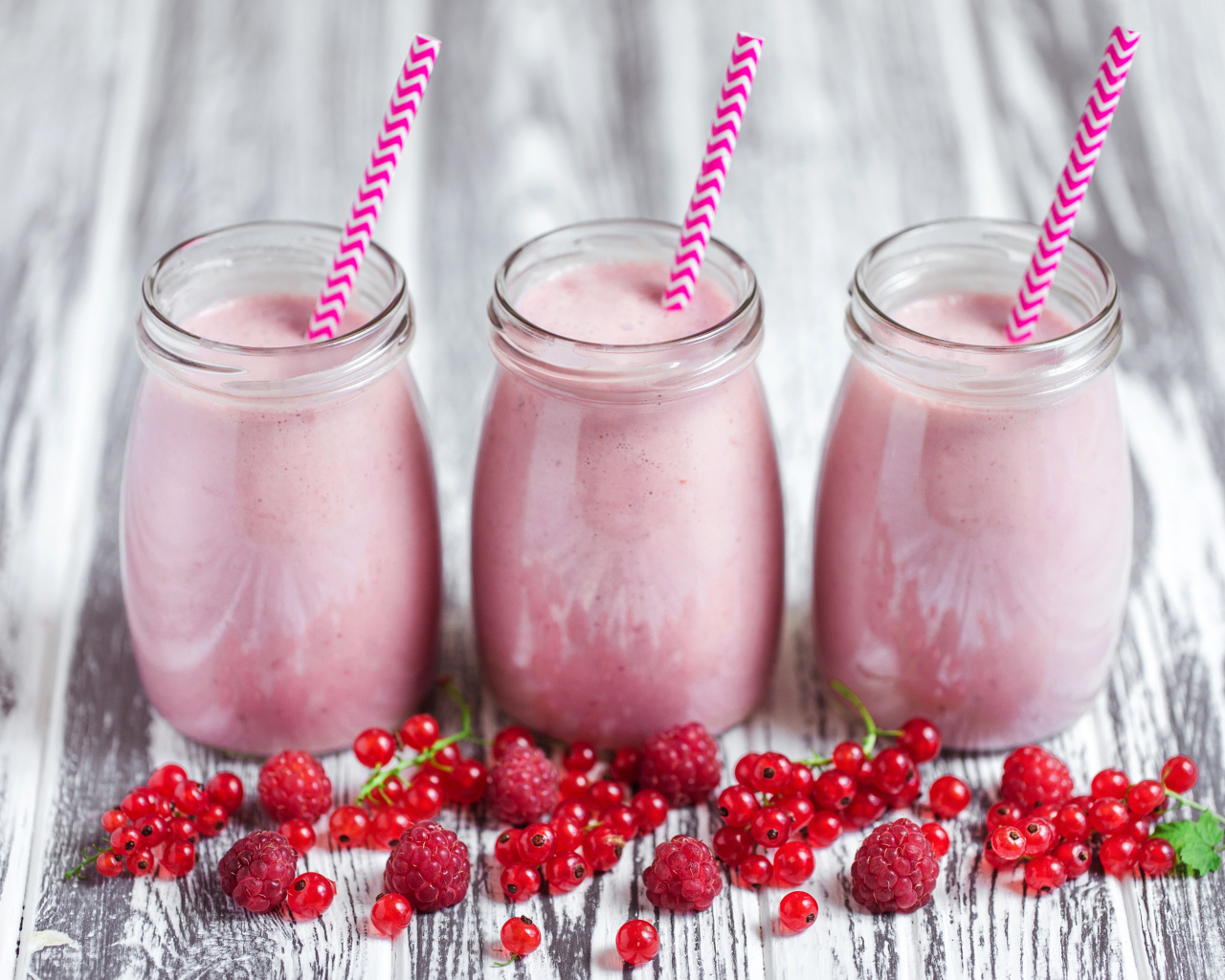 Три банки ягодного  смузи на столе с ягодами малины и смородины