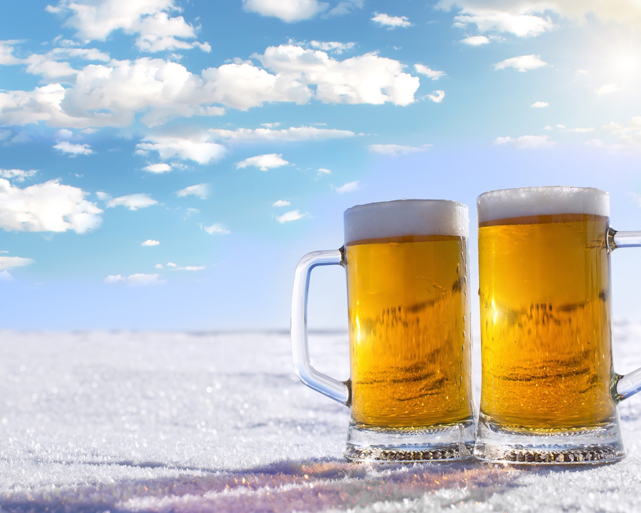 Два бокала пива стоят на белом снегу под голубым небом