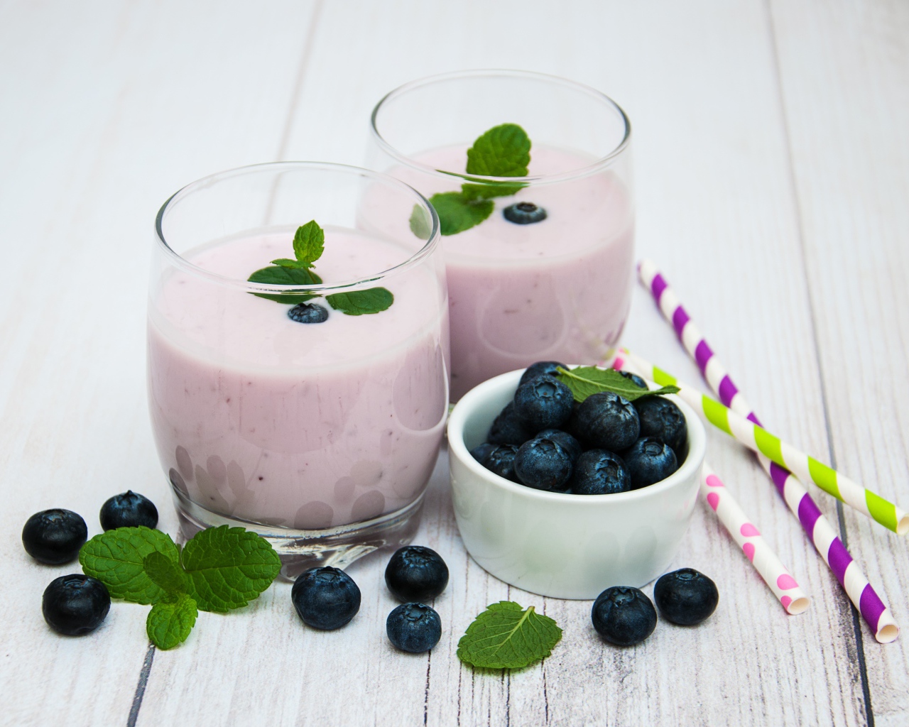 Два стакана коктейля в стаканах на столе с ягодами черники и трубочками