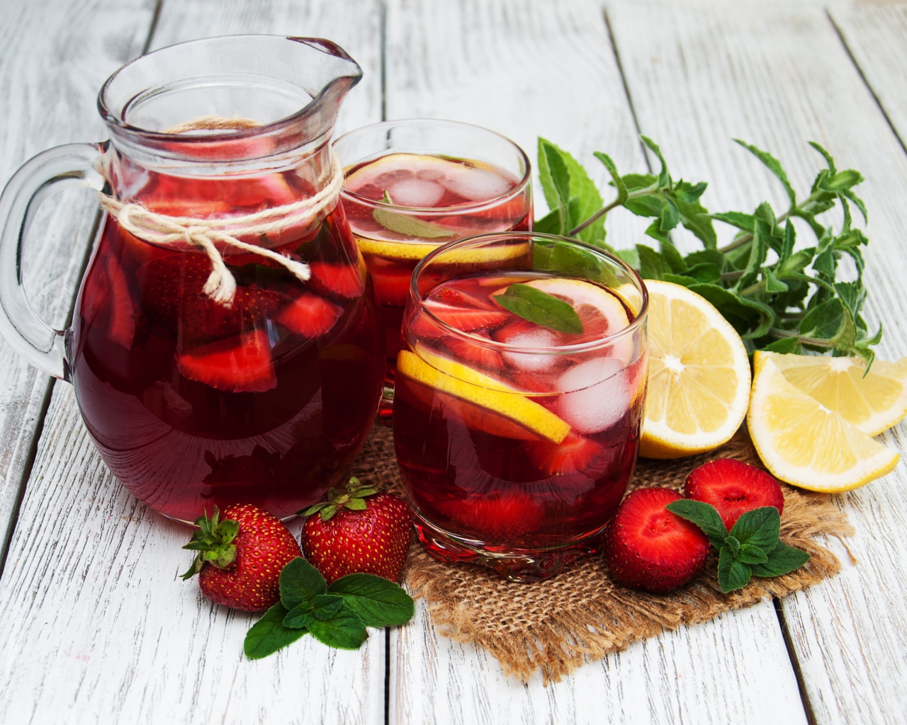 Два стакана мохито на столе с графином, лимоном, клубникой и мятой