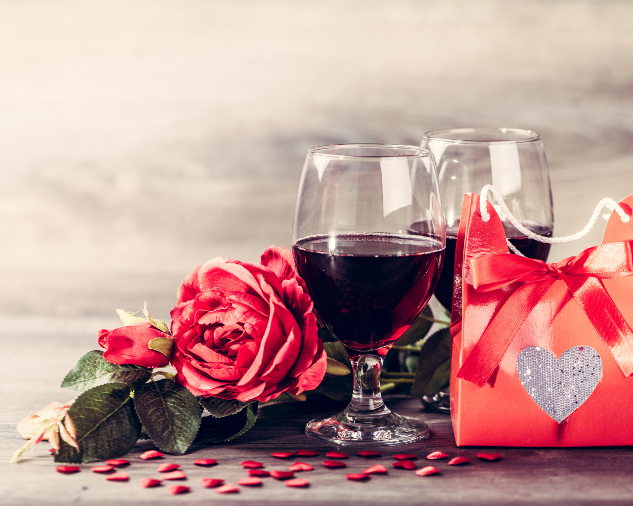 Два бокала красного вина на столе с розой и подарком 