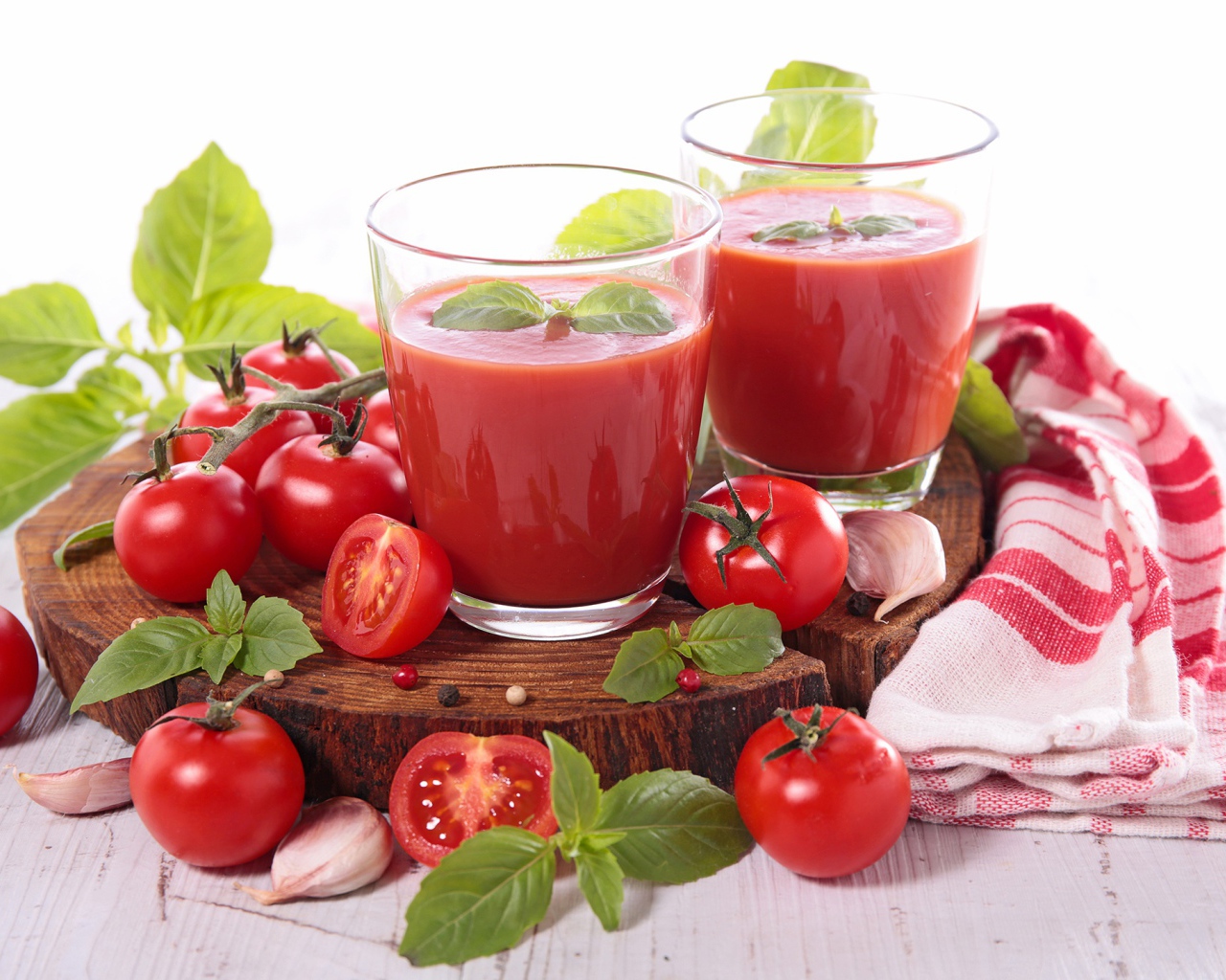 Два стакана томатного сока на столе с помидорами и зеленью 