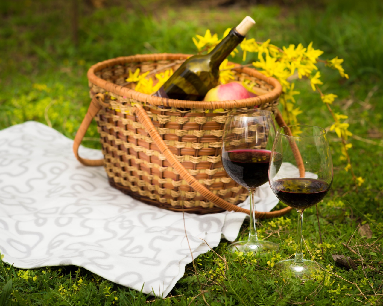 Два бокала вина с корзиной на зеленой траве для пикника 