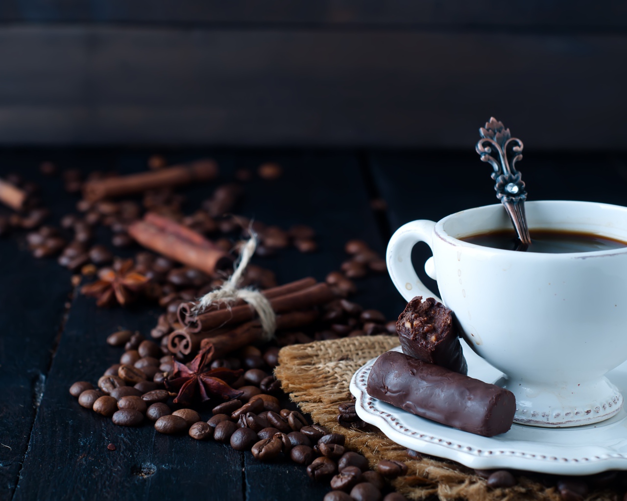 Белая чашка кофе на столе с конфетами, корицей, бадьяном и зернами