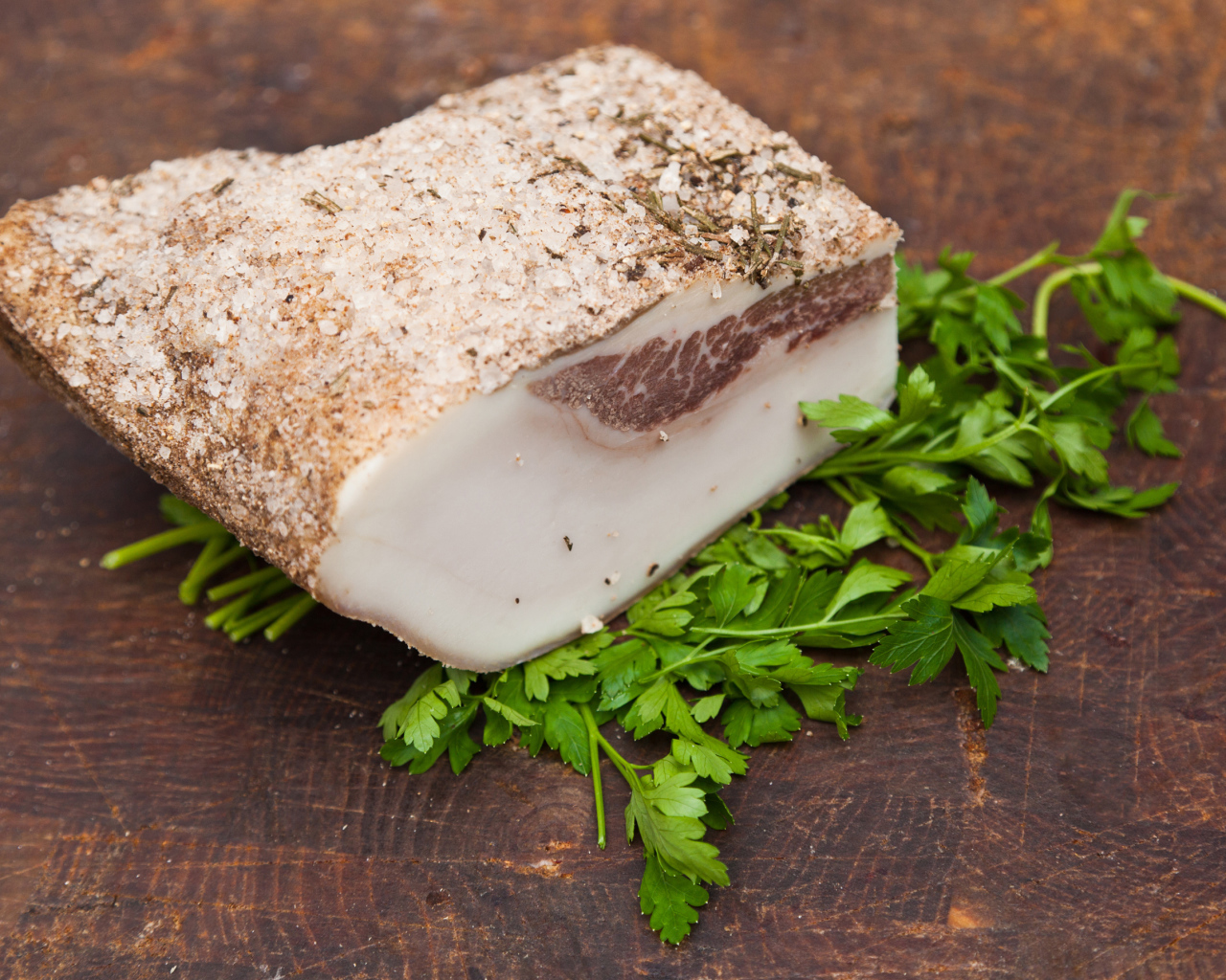 Кусок сала со специями на столе с зеленью петрушки