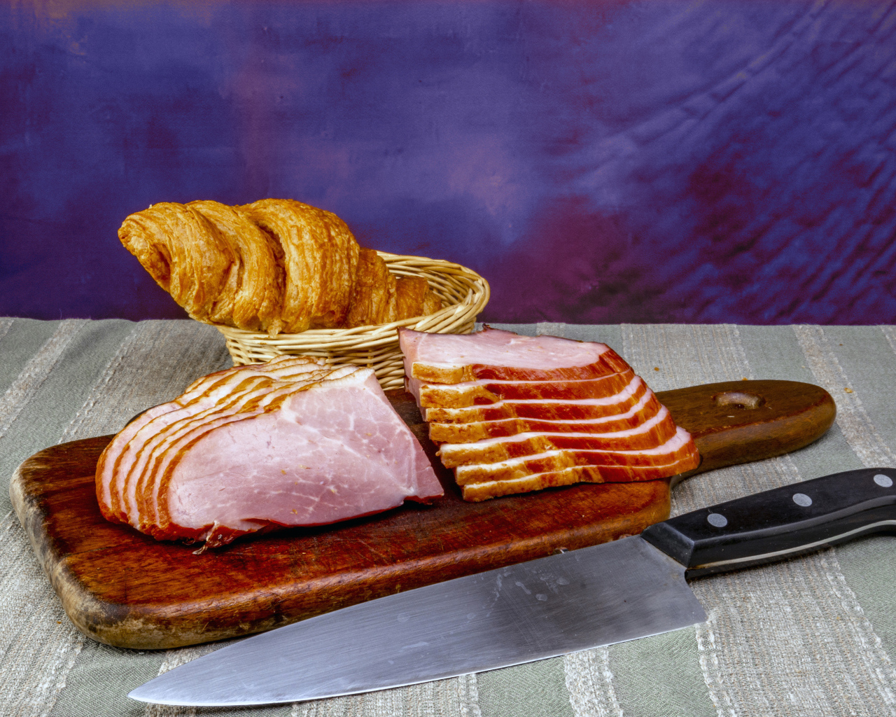 Кусок нарезанной ветчины на доске с круассаном