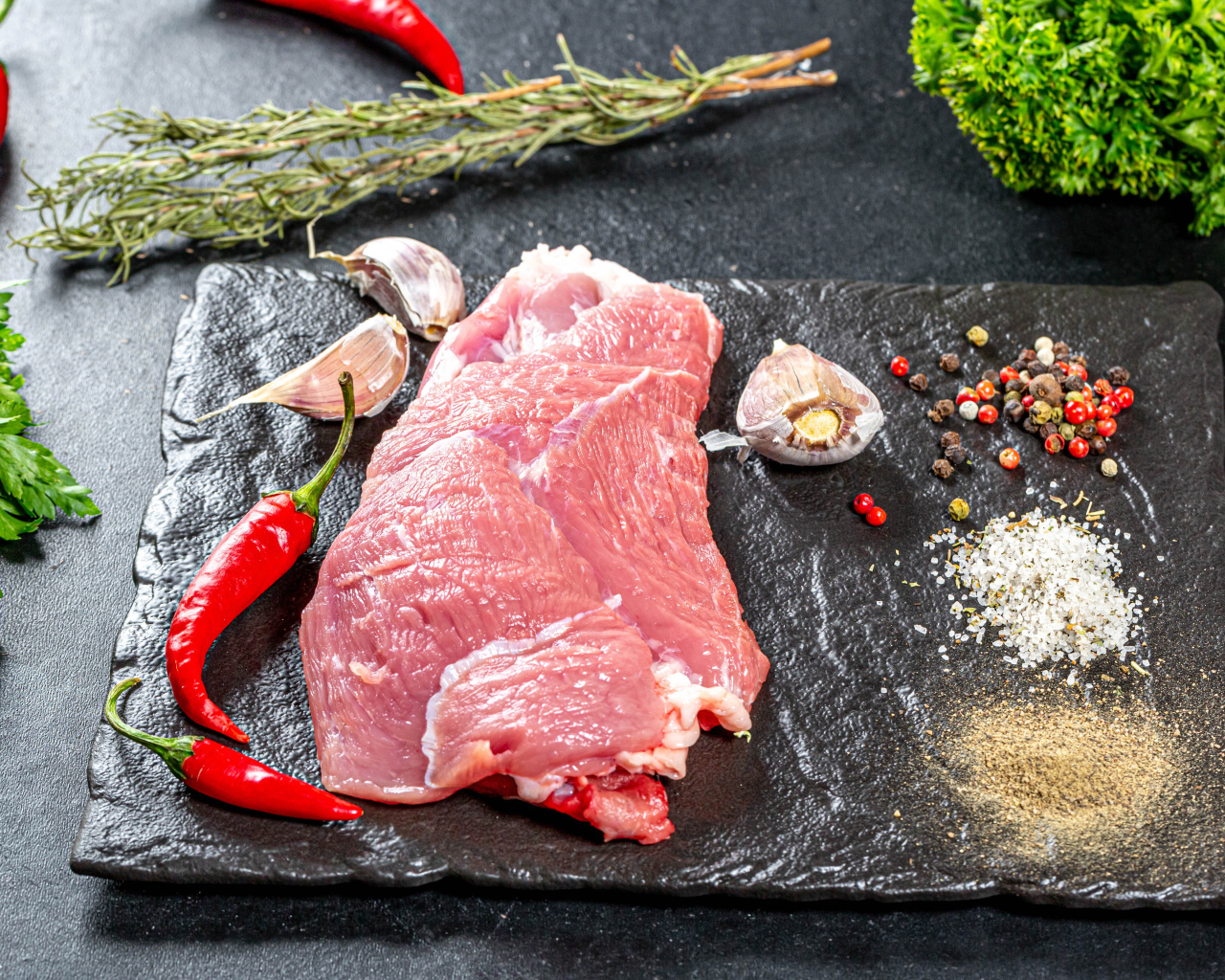 Кусок мяса на столе с острым перцем, чесноком и зеленью