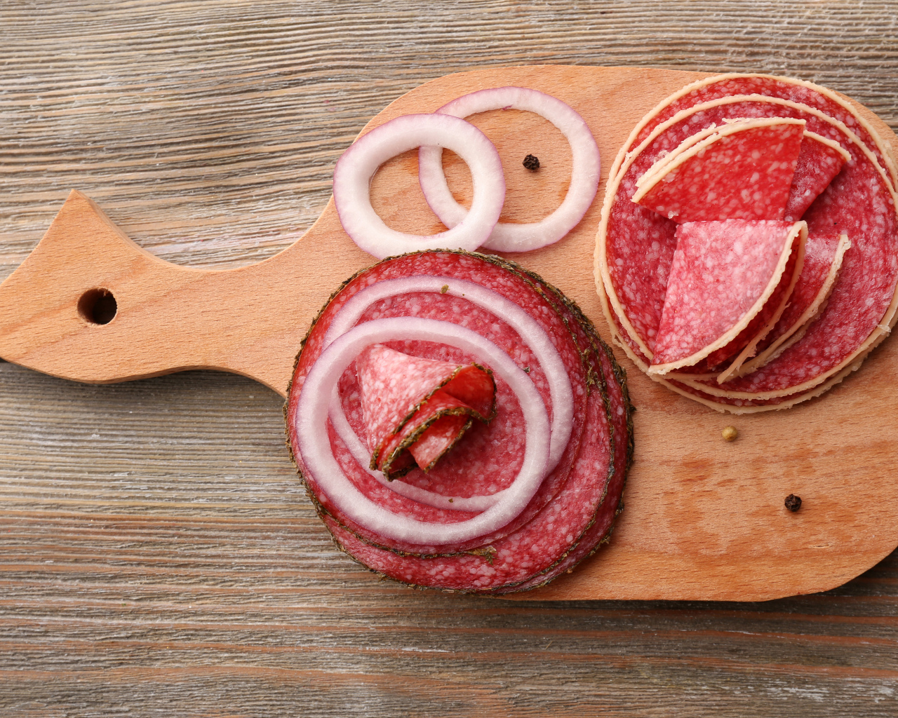 Аппетитные кусочки колбасы на разделочной доске с кольцами лука